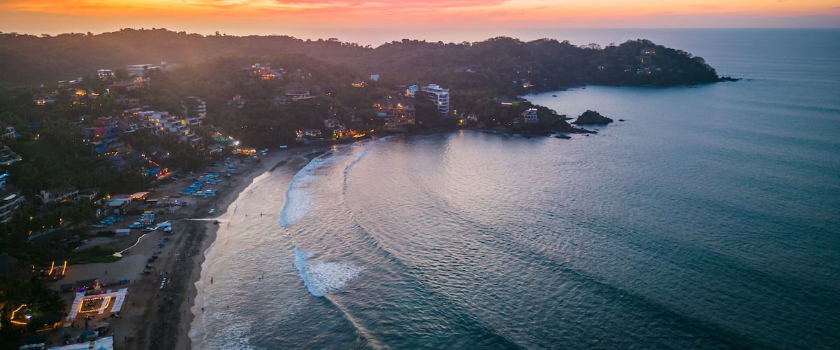 A coastal town with a beach, ocean, and a sunset sky.