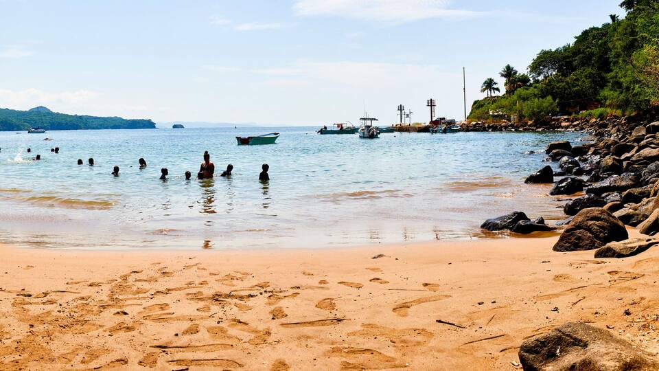 A beach with clear water, rocks, and boats.