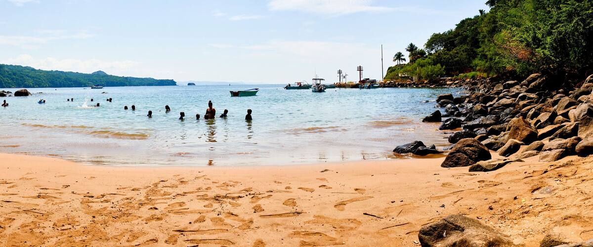 A beach with clear water, rocks, and boats.