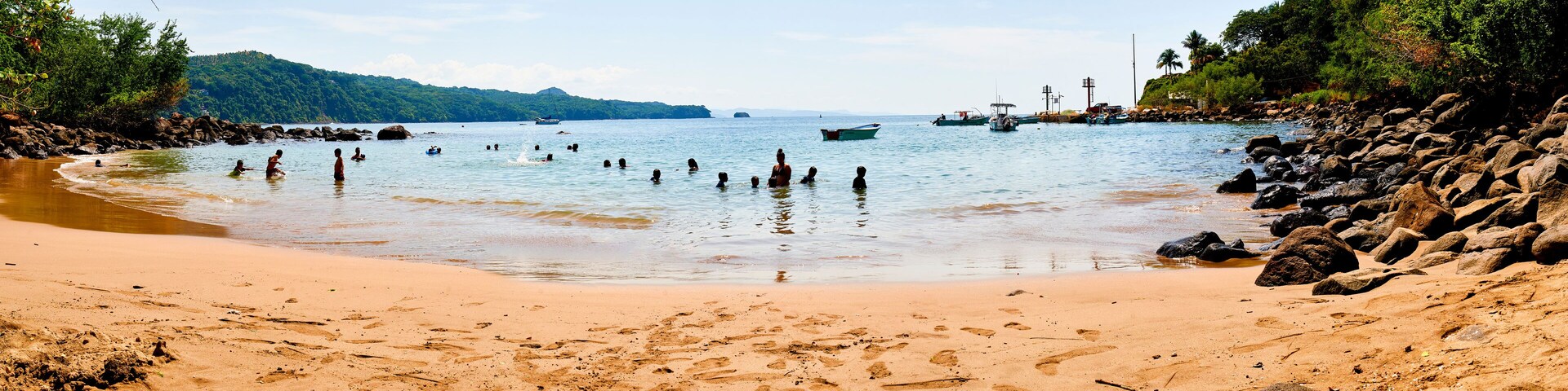 A beach with clear water, rocks, and boats.