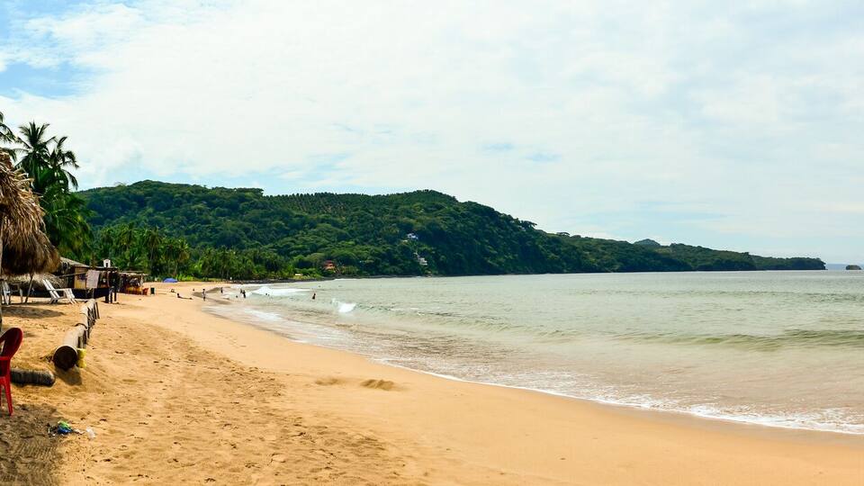 A beach with a clear view of the ocean, a sandy shore, and a small island with vegetation and buildings in the background.