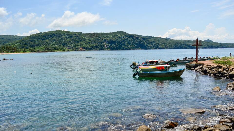 A calm lake with boats docked along the shore, surrounded by lush green hills.