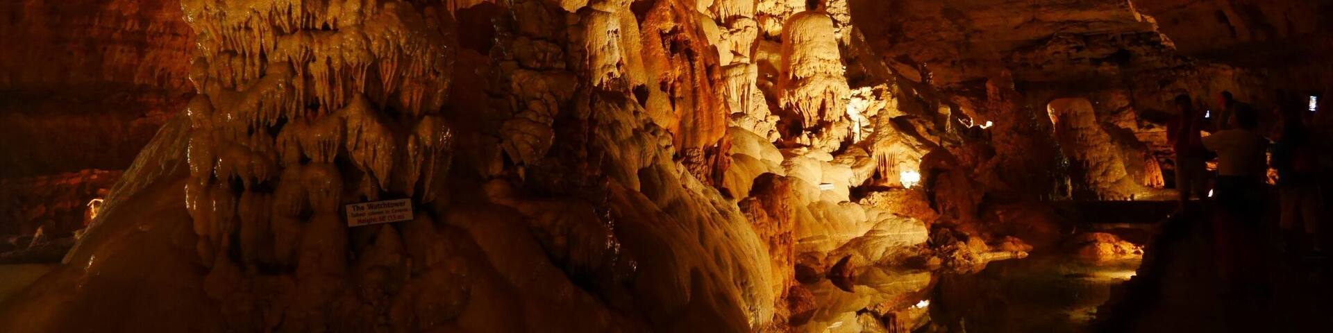 A cave with stalactites and stalagmites, illuminated by artificial lighting.