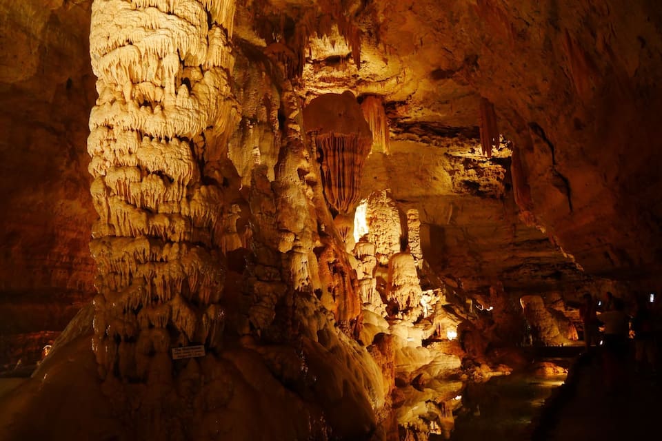 A cave with stalactites and stalagmites, illuminated by artificial lighting.