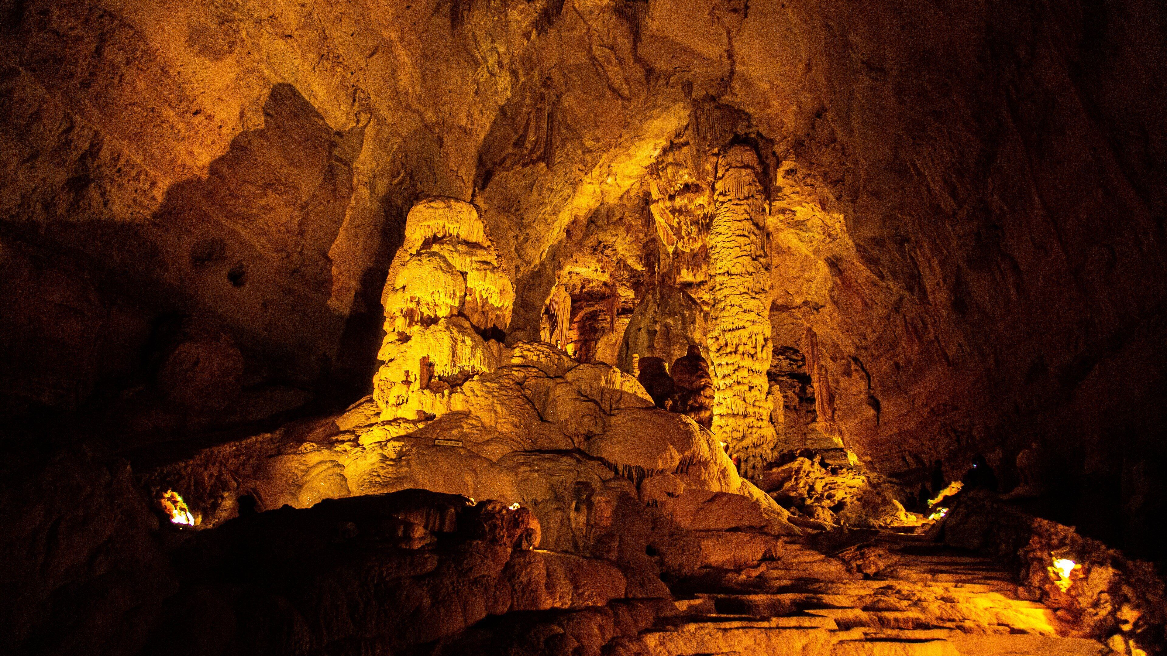 A cave with stalactites and stalagmites illuminated by artificial lighting.