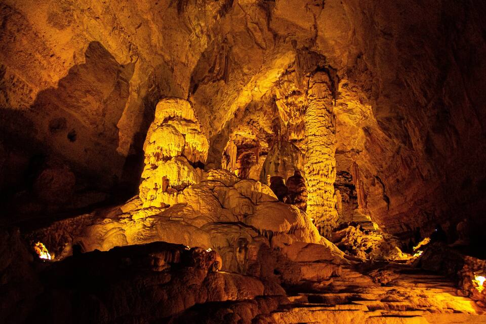 A cave with stalactites and stalagmites illuminated by artificial lighting.