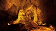 A cave with stalactites and stalagmites illuminated by artificial lighting.