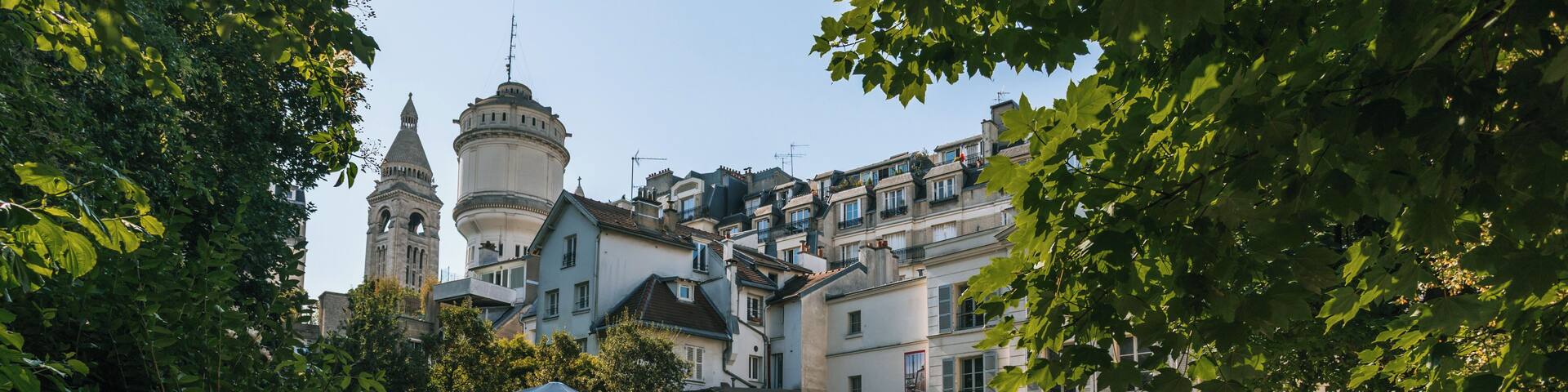A courtyard with a fountain, surrounded by lush greenery and historic buildings with a prominent tower.