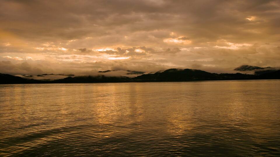 A calm lake with mountains in the background and a cloudy sky.