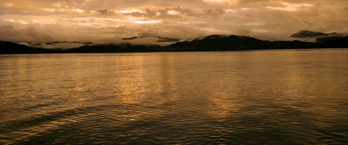 A calm lake with mountains in the background and a cloudy sky.
