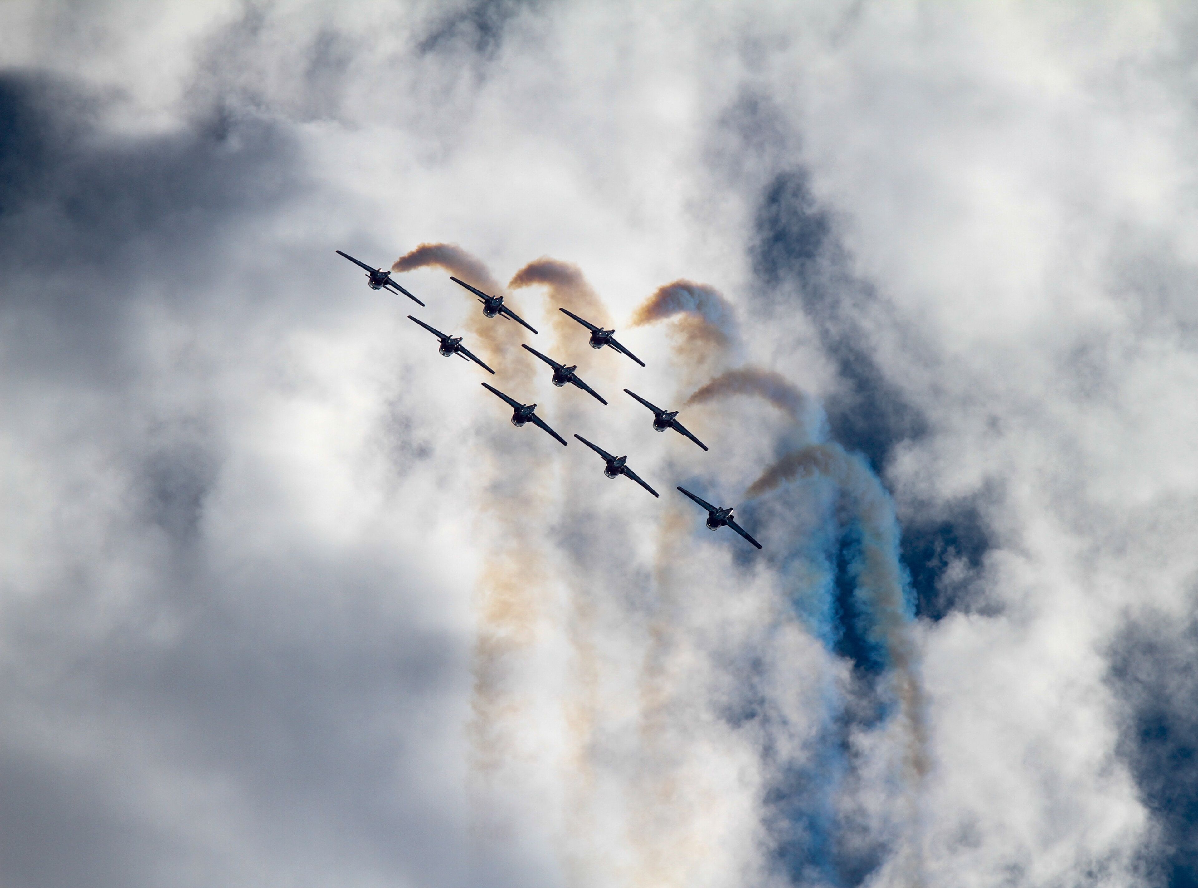 Silhouette of Airshow Fighter Jet airplanes in formation through big white clouds and a bright blue sky.  