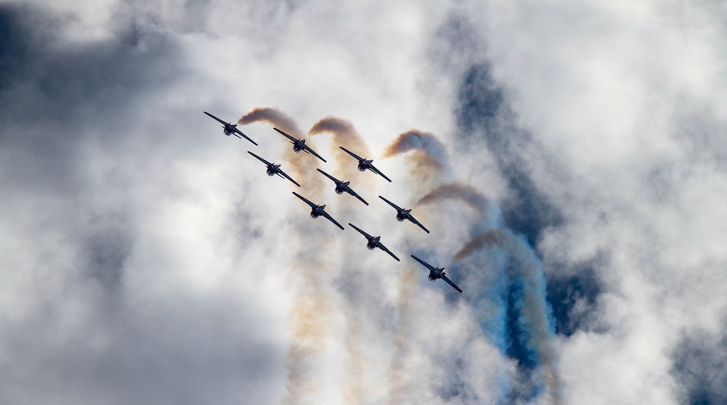 Silhouette of Airshow Fighter Jet airplanes in formation through big white clouds and a bright blue sky.