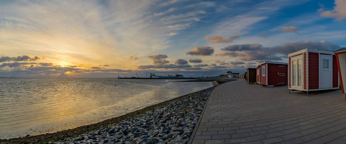 A waterfront promenade with beach huts and a sunset over the water.