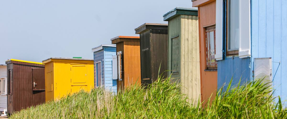 A row of colorful beach huts with a grassy foreground.