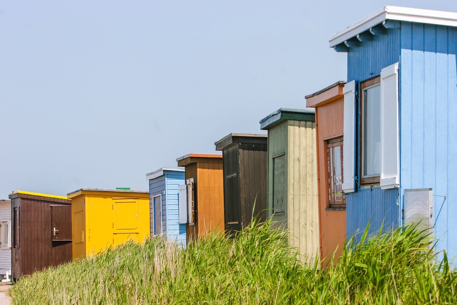 Een rij kleurrijke strandhutten met een grasveld op de voorgrond.