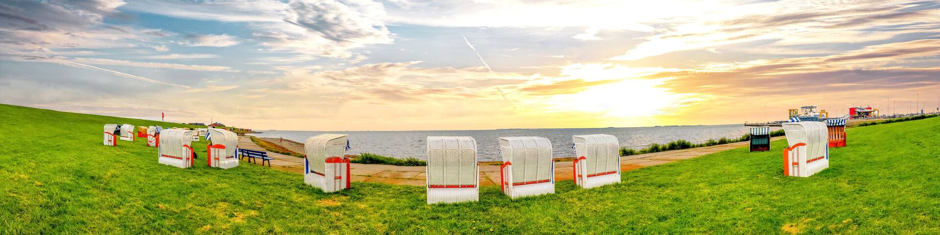 A grassy field with white beach chairs and a bench, overlooking a body of water with a sunset in the background.