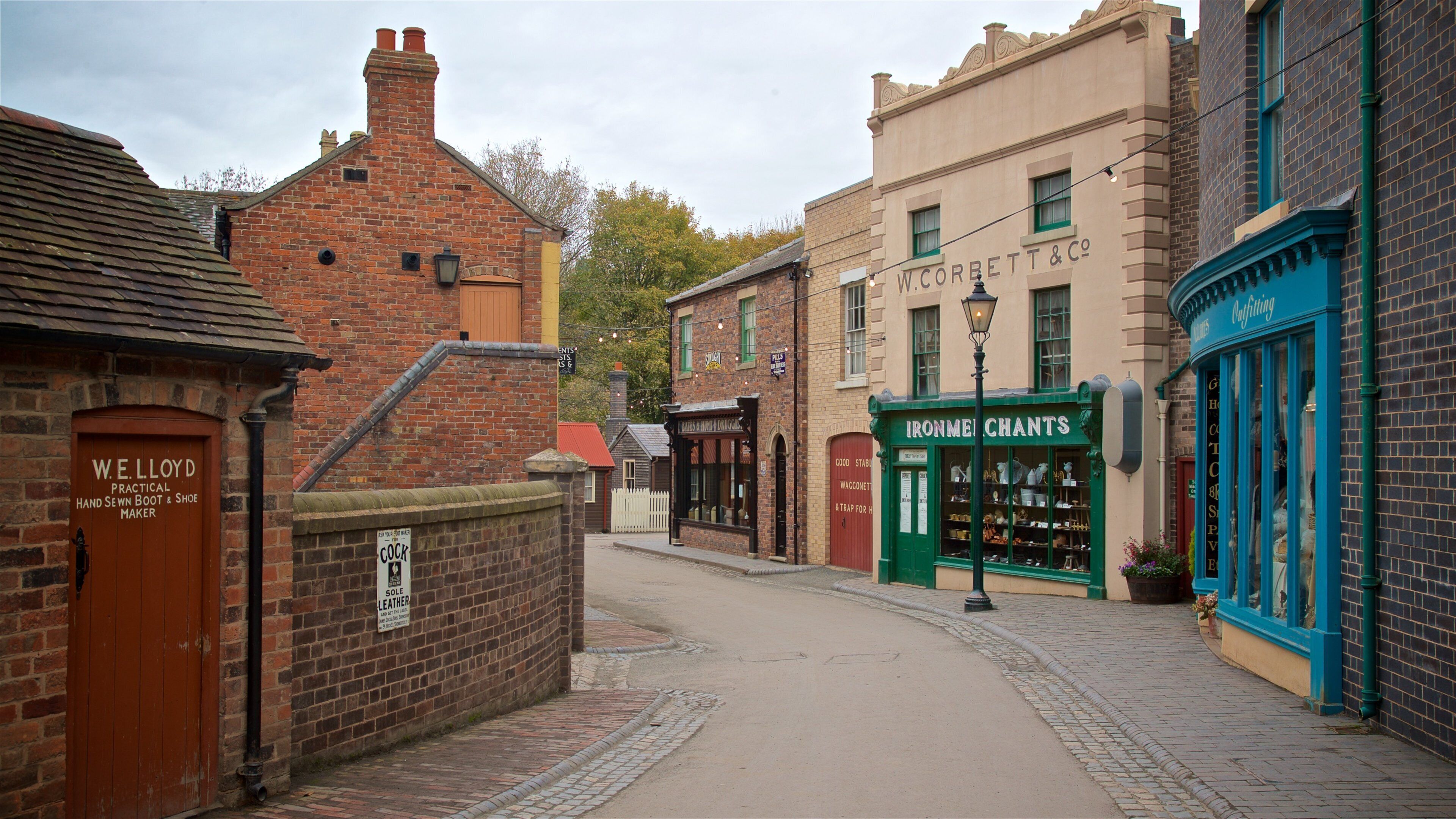 A narrow street lined with historic buildings, including a shoe maker and an iron merchant.