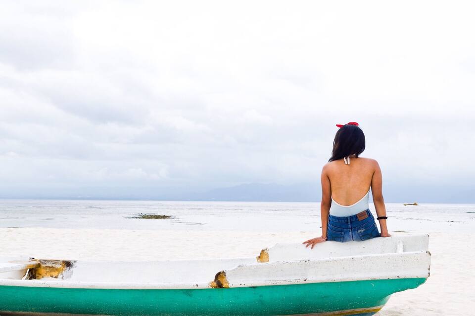 Une femme se tient debout sur un bateau, sur une plage, sous un ciel nuageux.