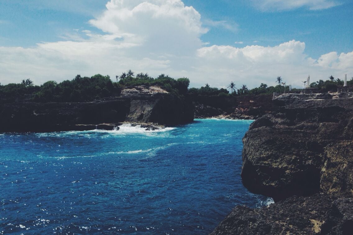 A coastal landscape with rocky cliffs, clear blue waters, and palm trees.