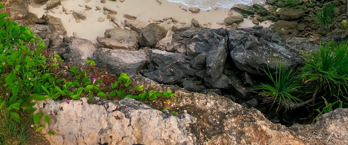 A coastal landscape with clear turquoise waters, rocky cliffs, and a sandy beach.
