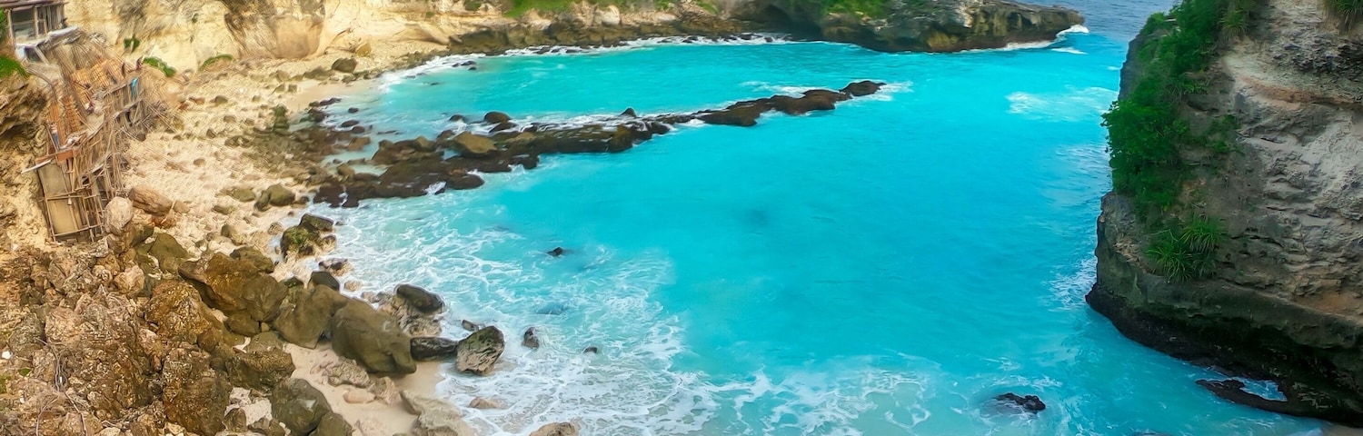 A coastal landscape with clear turquoise waters, rocky cliffs, and a sandy beach.