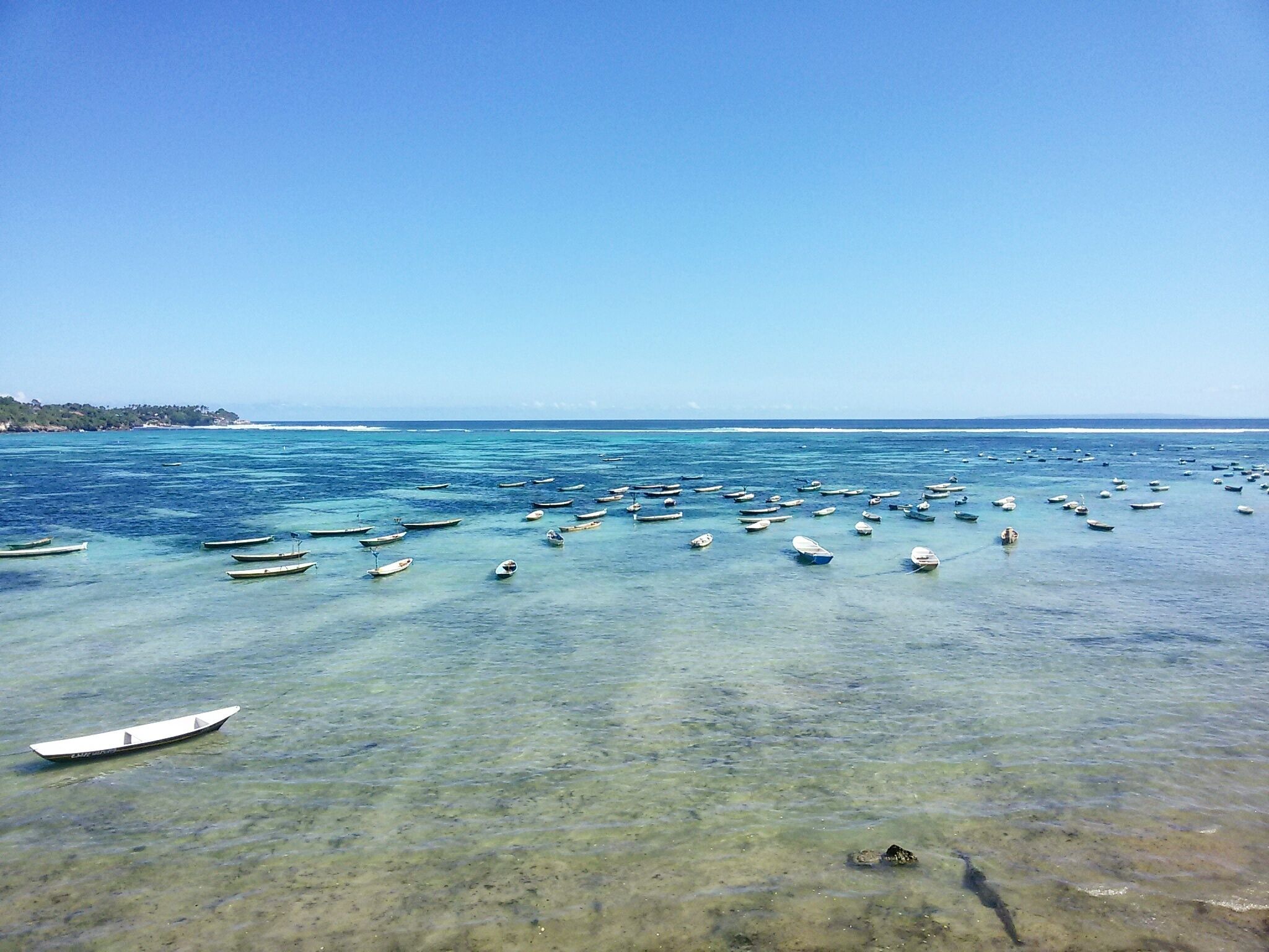 A coastal scene with numerous small boats anchored in clear shallow waters.
