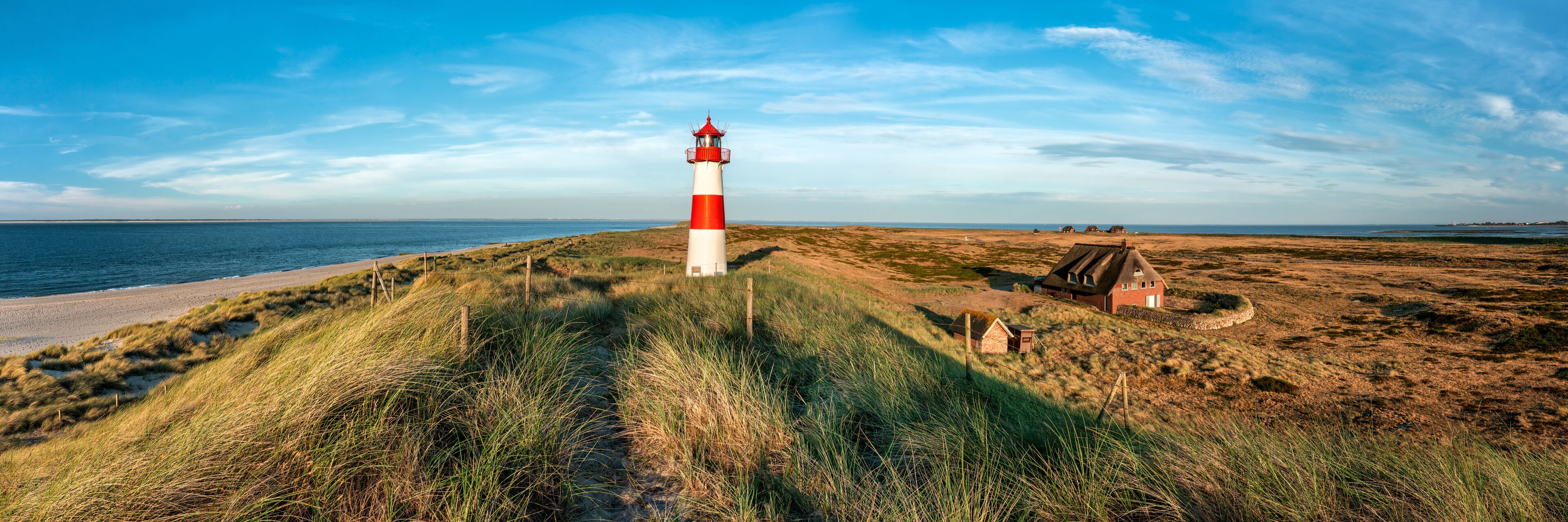 A red and white lighthouse on a grassy dune by the sea.