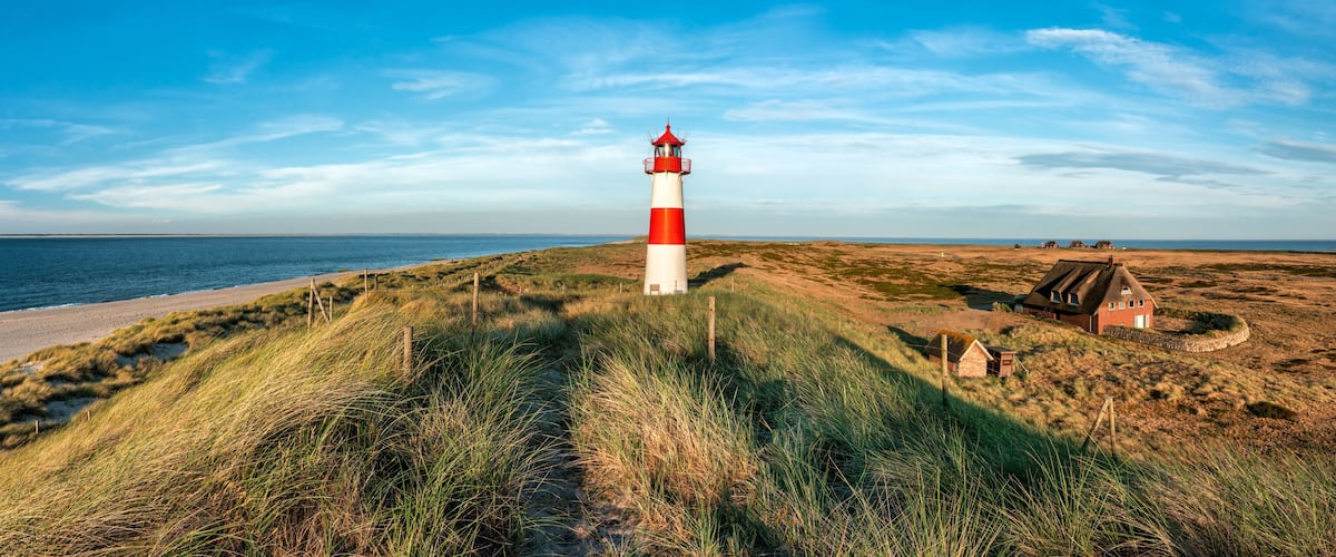 A red and white lighthouse on a grassy dune by the sea.