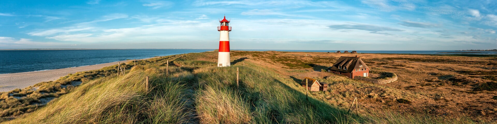 A red and white lighthouse on a grassy dune by the sea.
