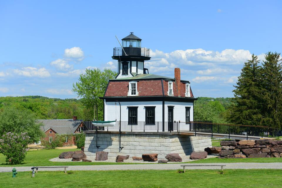 A lighthouse with a white and black exterior, a stone base, and a surrounding stone wall.