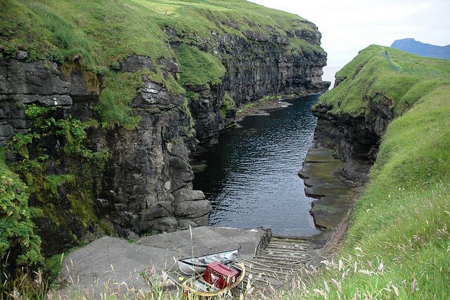 A narrow waterway flanked by steep, grassy cliffs.
