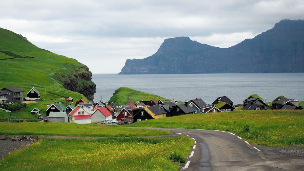 The village of Gjogv sits right on the coast of Eysturoy, with a small gorge nearby and imposing flat-topped mountains in the distance.
