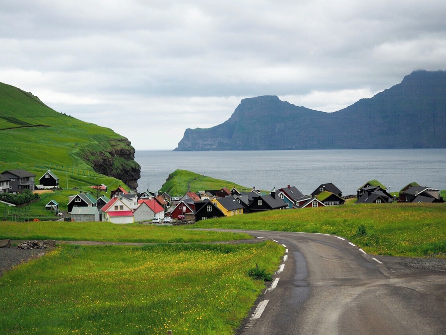 The village of Gjogv sits right on the coast of Eysturoy, with a small gorge nearby and imposing flat-topped mountains in the distance.