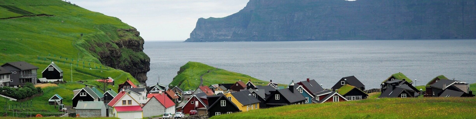 The village of Gjogv sits right on the coast of Eysturoy, with a small gorge nearby and imposing flat-topped mountains in the distance.
