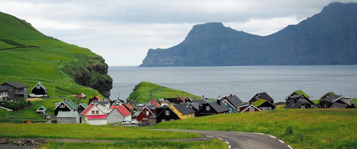 A coastal village with houses on grassy hills and a road curving through the landscape.