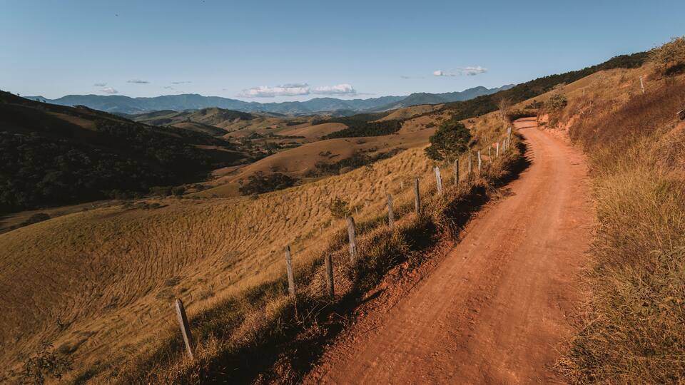 A dirt road winding through a hilly landscape with sparse vegetation and distant mountains.
