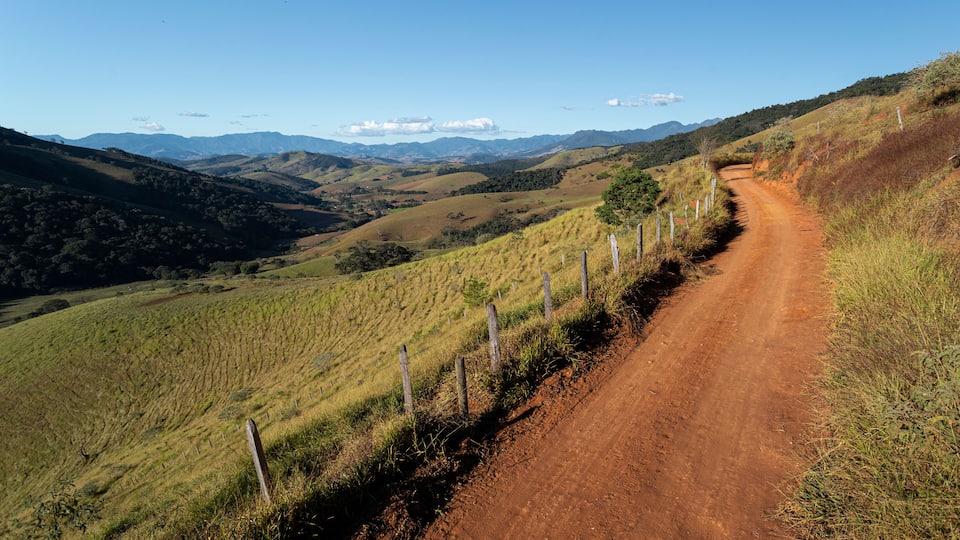 A dirt road winding through rolling hills with sparse vegetation and a clear blue sky.