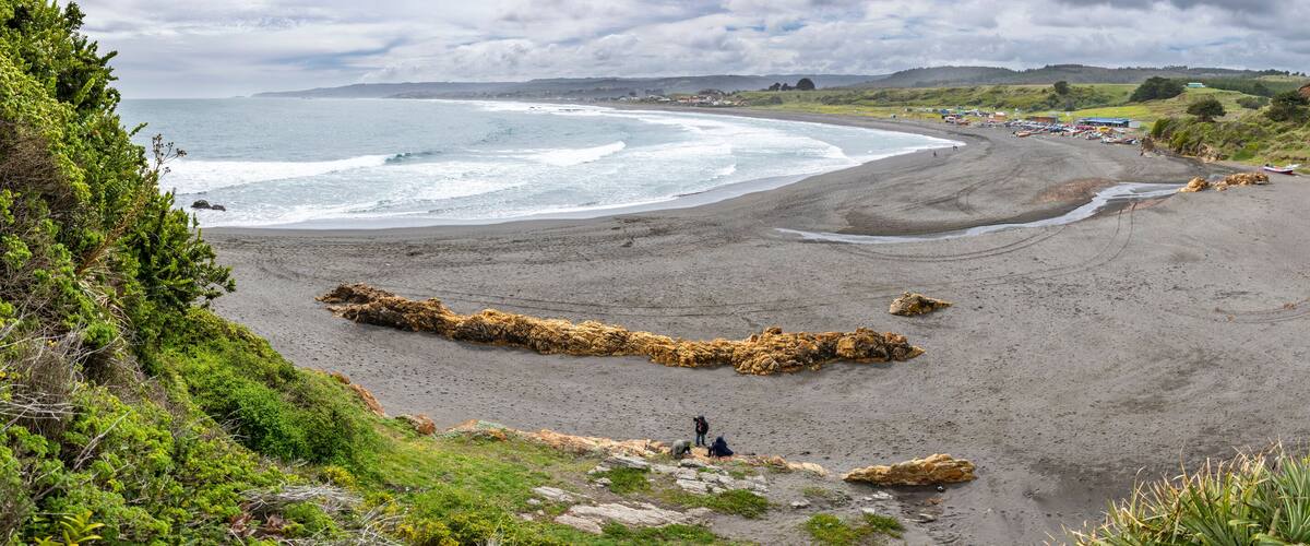 A coastal landscape with a sandy beach, rocky outcrops, and a distant shoreline.