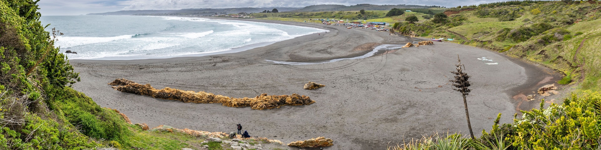 A coastal landscape with a sandy beach, rocky outcrops, and a distant shoreline.