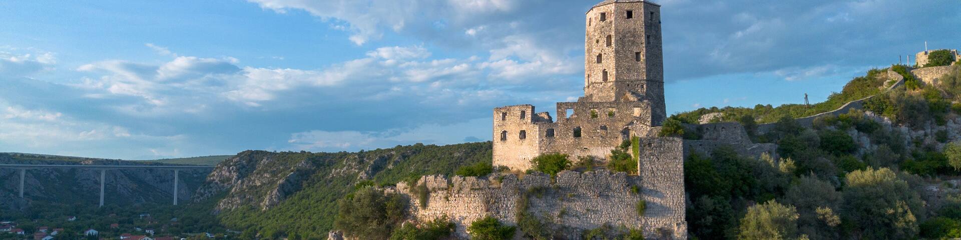 A historic stone castle on a hill with a bridge in the background.