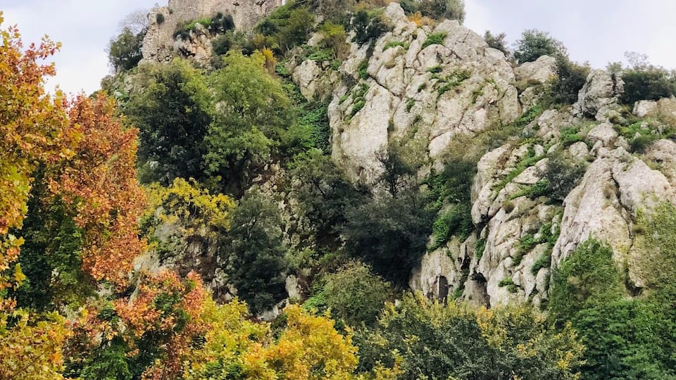 A historic stone tower atop a rocky hill, surrounded by autumn-colored trees.