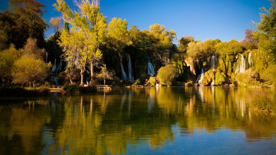 A serene lake with multiple waterfalls surrounded by lush trees.