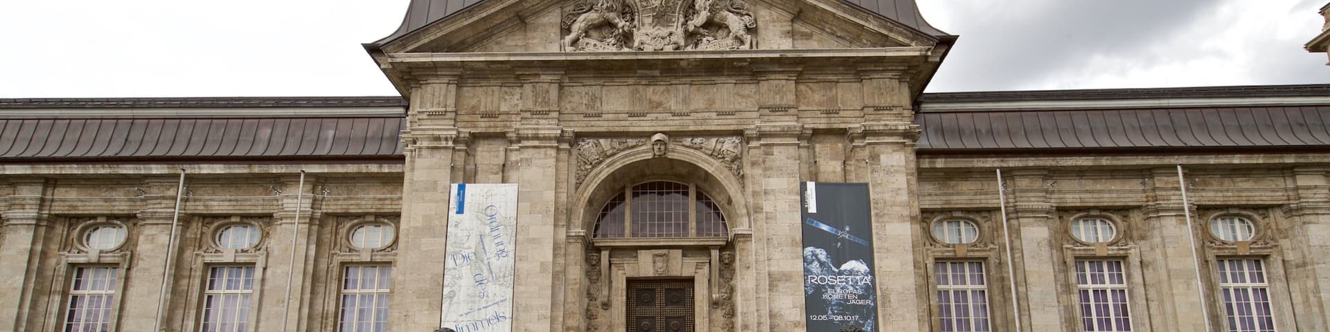 A historic building with a grand entrance, large columns, and a prominent statue.