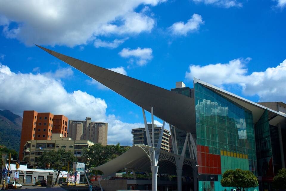 A modern urban landscape with a prominent glass building, a large wing-like structure, and a mountain in the background.