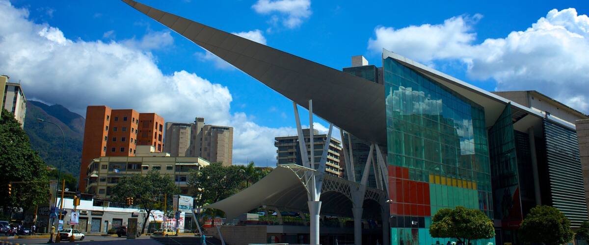 A modern urban landscape with a prominent glass building, a large wing-like structure, and a mountain in the background.