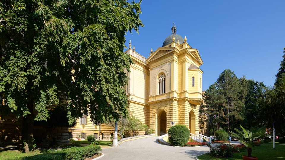 A yellow building with a dome and arched windows, surrounded by trees and a paved walkway.