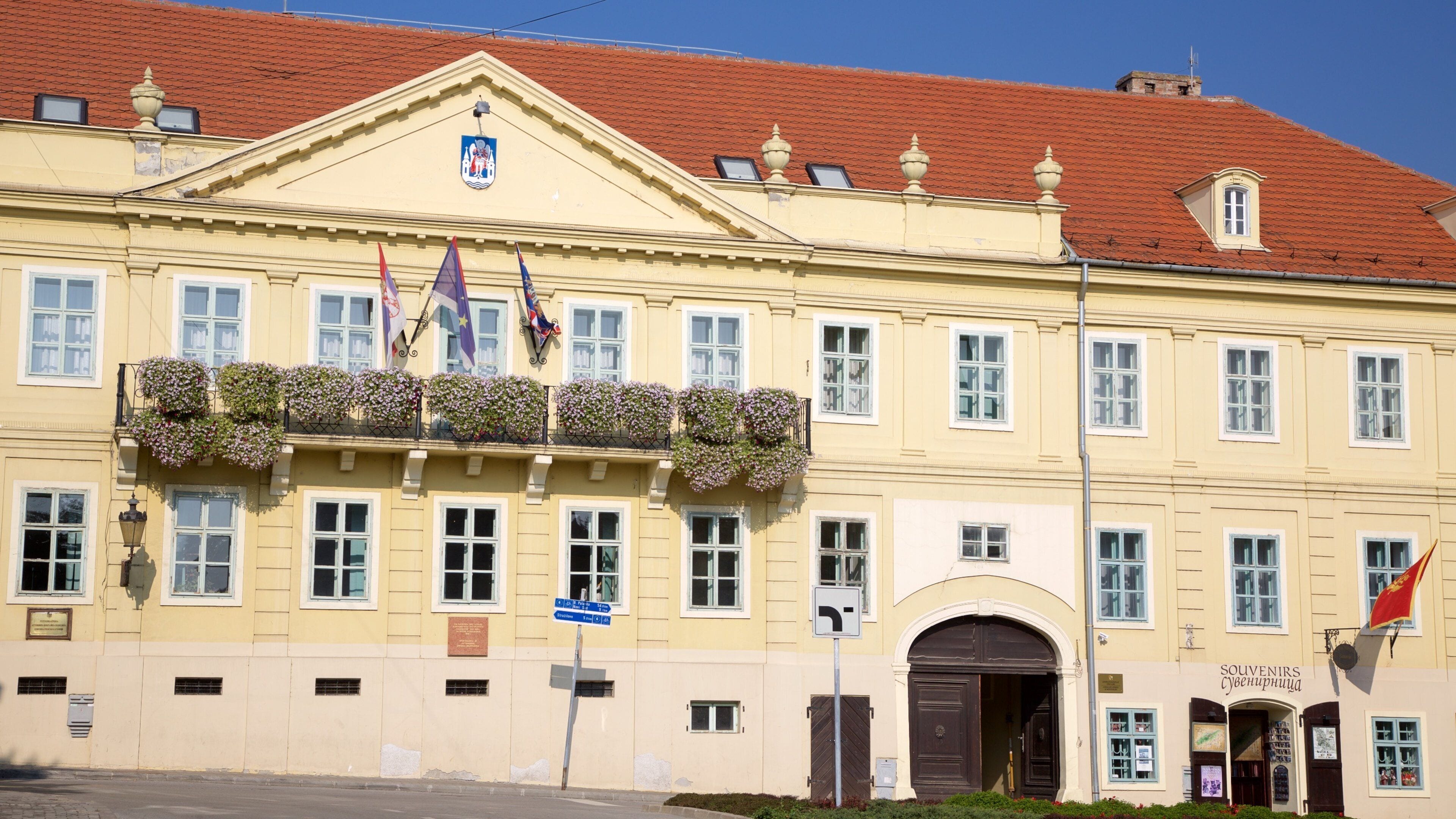 A historic building with a yellow facade, red tiled roof, and multiple flags.