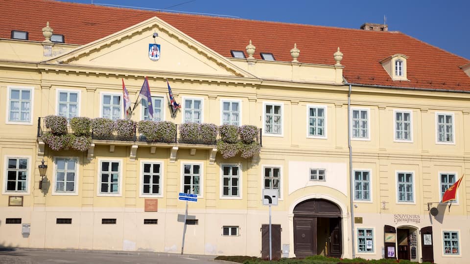 A historic building with a yellow facade, red tiled roof, and multiple flags.