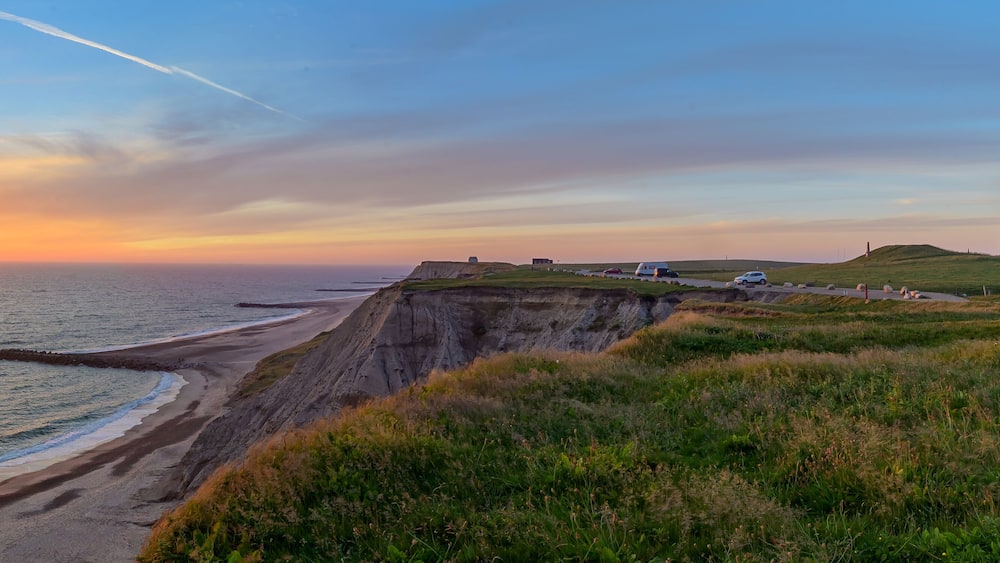 Un coucher de soleil sur la côte, avec un phare, des falaises et une route.