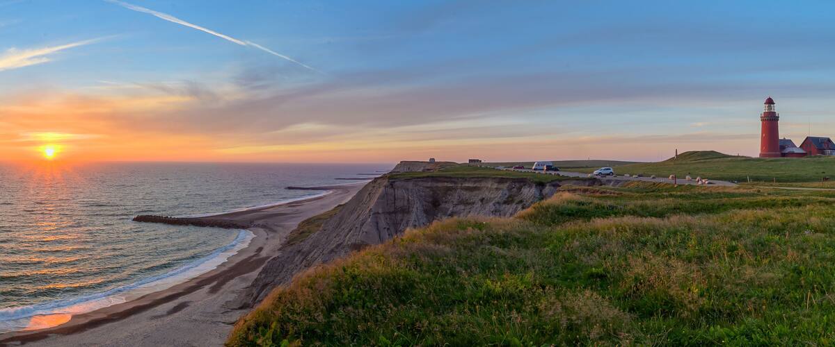 A coastal sunset with a lighthouse, cliffs, and a road.